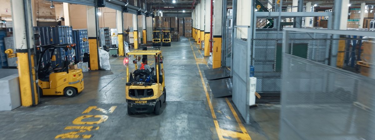 Pasillo central de bodega con montacargas en operación